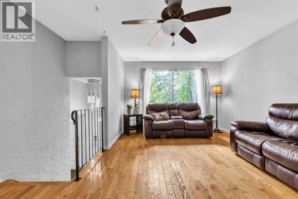 Living room with hardwood floors, brown leather sofas, floor lamps, and a large window with curtains. - 215 Erin Woods Drive Se, Calgary