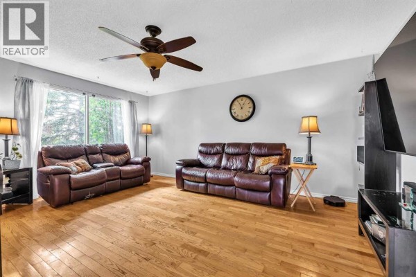 Spacious living room featuring polished hardwood floors, plush leather seating, a ceiling fan, and a wall clock. - 215 Erin Woods Drive Se, Calgary
