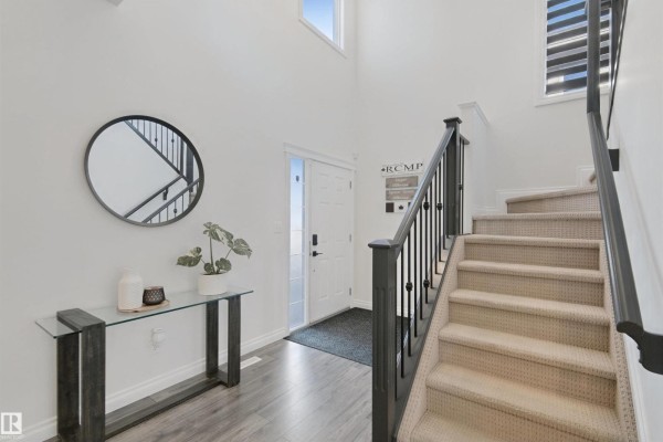 Entrance foyer with a high ceiling, staircase, round mirror, and glass console table. - 215 Henderson Li, Spruce Grove