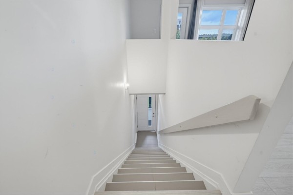 White staircase with a light gray handrail descends towards a door and a window. - 215 Rue De Dublin, #7, Gatineau