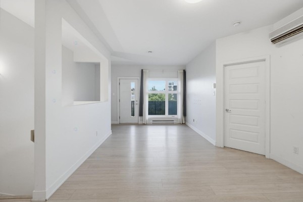 Bright, empty living room with light wood floors, white walls, and a large window. - 215 Rue De Dublin, #7, Gatineau