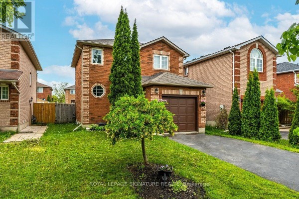 View of the front of a brick house with a manicured lawn, green trees, and an asphalt driveway. - 215 Turnbridge Road, Barrie