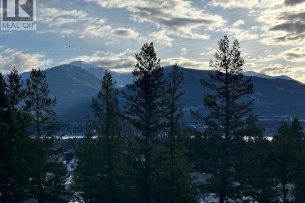 Distant mountains under a cloudy sky, viewed through evergreen trees. - 2151 Pineridge Drive Lot# 27, Invermere