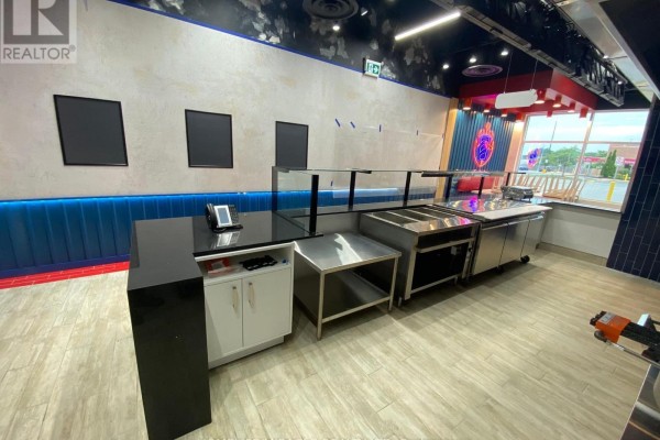 Restaurant service counter with a black countertop, stainless steel prep areas, and modern seating. - 2151 St. Clair Avenue, Toronto