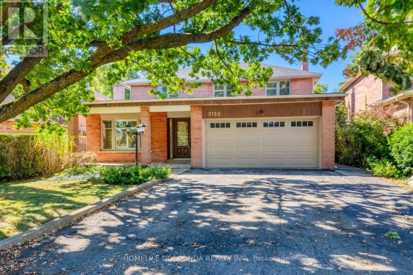 Front view of a red brick house with mature trees and a paved driveway. - 2152 Munn's Avenue, Oakville