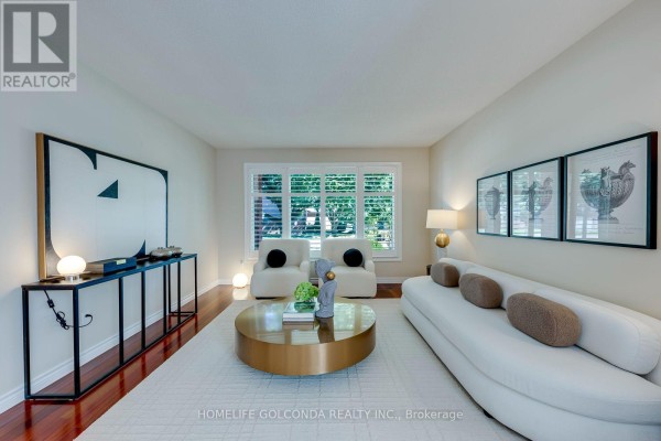 Living room with a white curved sofa, modern armchairs, a round gold coffee table, and large artwork. - 2152 Munn's Avenue, Oakville