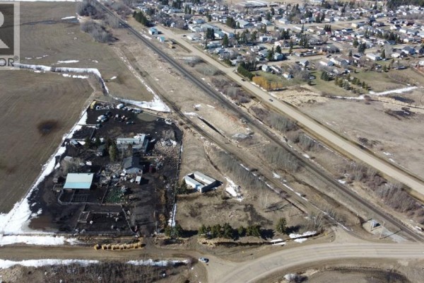Aerial view showing buildings and yards on a property next to railway tracks and a highway, with a town in the distance. - 21528a Sec Hwy  617, Rural Camrose County