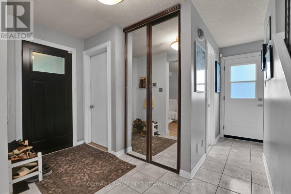 Entrance hallway with a black front door, tiled floor, and a large mirrored closet. - 2153 East Acres Road, Ottawa