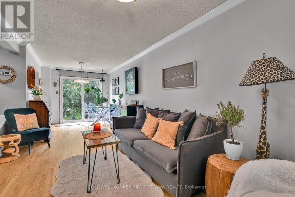 Living room with a grey sofa, light wood floors, and a glass sliding door leading outside. - 2153 East Acres Road, Ottawa