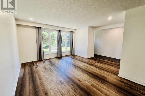 Interior view of a spacious room with white walls, dark wood laminate flooring, and large windows. - 2154 Adullam Avenue, Innisfil
