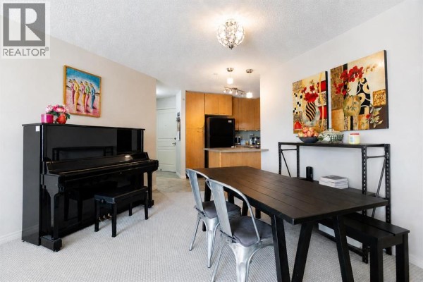 Dining area and kitchen with light wood cabinets, black appliances, and a large floor mirror. - 216, 5115 Richard Road Sw, Calgary