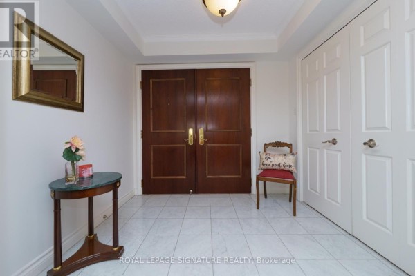 Foyer with tiled floor, a dark wood double door entrance, a small round table, and a mirror. - 216 - 215 The Donway West W, Toronto