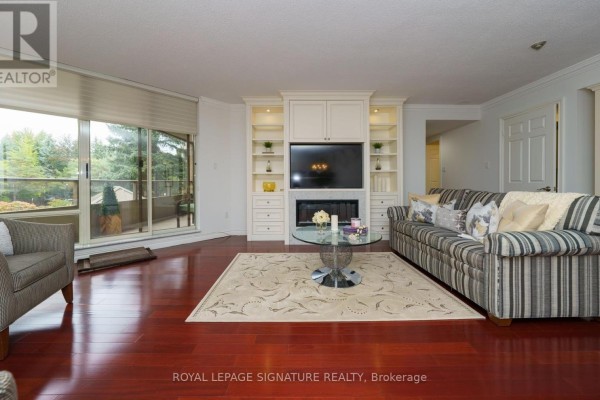 Living room with fireplace, built-in shelving, striped sofa, patterned rug, and large sliding glass doors. - 216 - 215 The Donway West W, Toronto