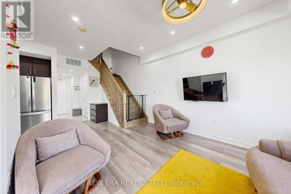 Living area with light wood floors, grey chairs, television, and wooden stairs. - 216 - 3865 Major Mackenzie Drive W, Vaughan