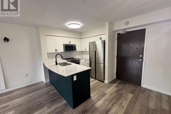 Modern kitchen featuring white cabinetry, a dark green island, and stainless steel appliances. - 216 - 40 Via Rosedale Avenue, Brampton