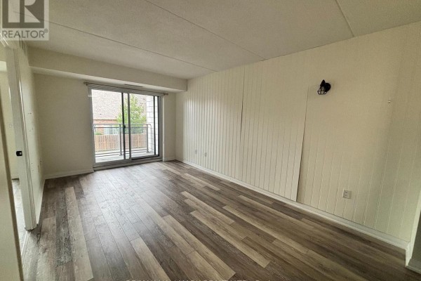 Living room with wood-look flooring and a sliding glass door leading to a balcony. - 216 - 40 Via Rosedale Avenue, Brampton