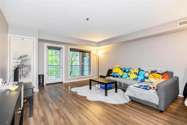 Living room with grey sectional sofa, coffee table, wood floors, and balcony door. - 216 25 Bridgeland Drive, Winnipeg