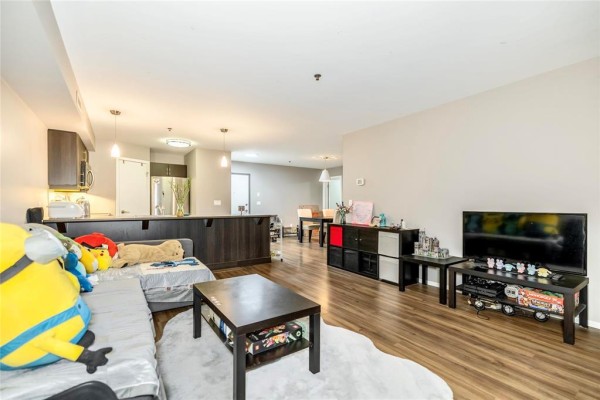 Open concept living area with grey sofa, coffee table, and kitchen island. - 216 25 Bridgeland Drive, Winnipeg