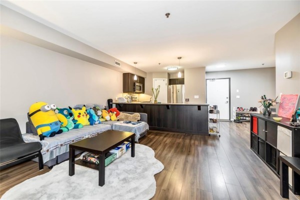 Living room and kitchen area with dark wood cabinets, island, and vinyl plank flooring. - 216 25 Bridgeland Drive, Winnipeg