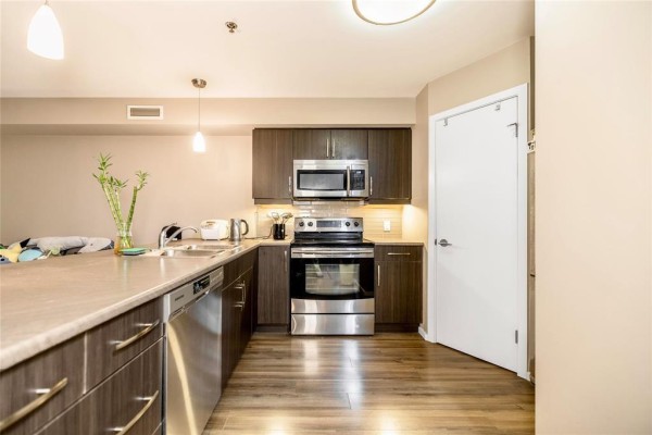 Kitchen with stainless steel appliances, dark wood cabinets, and island with sink. - 216 25 Bridgeland Drive, Winnipeg