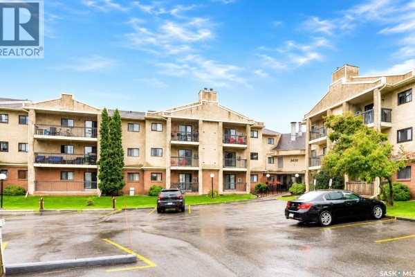 Apartment building exterior and parking lot with black and silver cars on a wet day. - 216 3420 Park Street, Regina