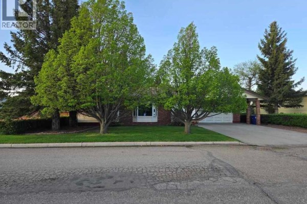 View of the front of the house from the street, with a manicured lawn and large mature trees. - 216 3rd Avenue E, Eatonia