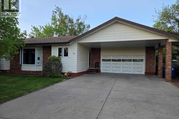 Side view of the house, showcasing the cream siding, brick accents, and attached carport with a garage door. - 216 3rd Avenue E, Eatonia