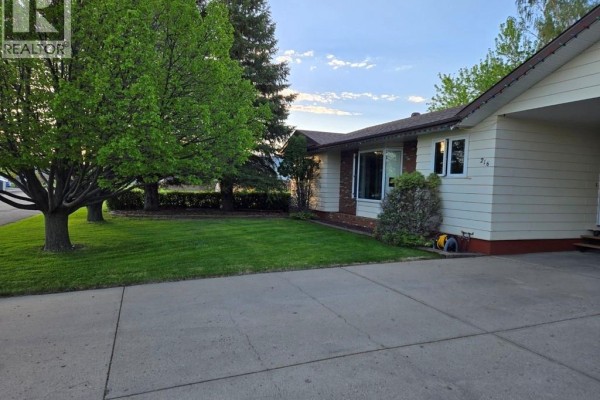 Exterior of the house with a focus on the lawn, large trees, and cream-colored siding with brick accents. - 216 3rd Avenue E, Eatonia