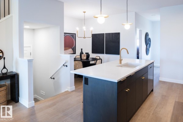 Island kitchen with dark cabinets and white countertop, overlooking a dining area with a round table. - 216 Chappelle Dr Sw, Edmonton