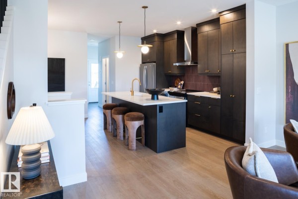 Kitchen island with stools and dark cabinets, with a view of the dining area and living room. - 216 Chappelle Dr Sw, Edmonton