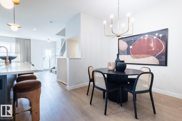 Dining area with a black round table, cane-backed chairs, and modern gold chandelier. - 216 Chappelle Dr Sw, Edmonton