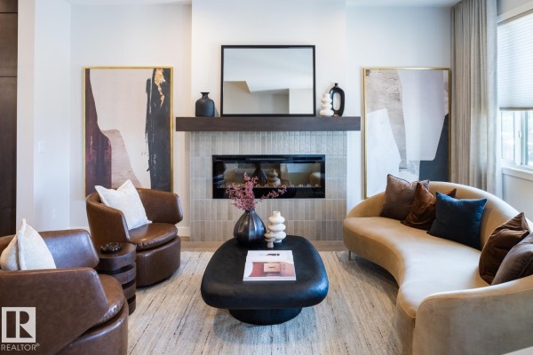 Living room with a fireplace, two sofas, two leather armchairs, and modern artwork. - 216 Chappelle Dr Sw, Edmonton