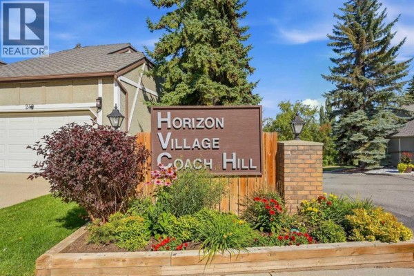 Sign for Horizon Village Coach Hill in a landscaped area with flowers and trees. - 216 Coach Side Road Sw, Calgary