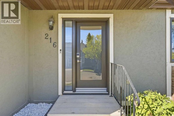 Front entrance of 216 Coach Side Road SW, Calgary, with a glass door and stucco exterior. - 216 Coach Side Road Sw, Calgary
