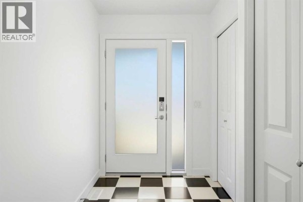 Interior entryway with a white door, frosted sidelight, and black and white checkered tile floor. - 216 Coach Side Road Sw, Calgary