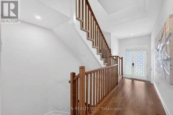 Hallway looking toward the front door with wood floors and a staircase. - 216 Trumpeter Grove, Ottawa