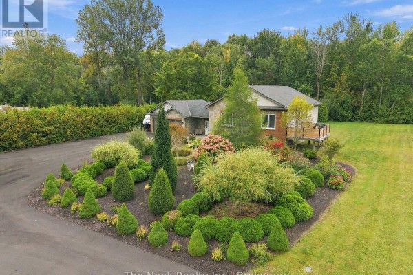 Manicured garden beds with shrubs and trees in front of a house. - 21611 Loyalist Parkway, Prince Edward County