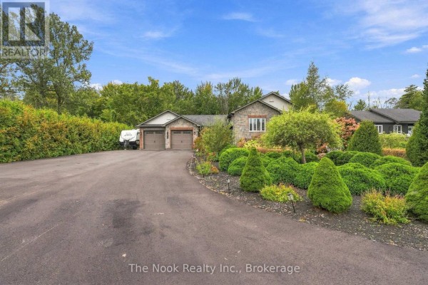 Wide shot of the house, garden, and driveway with surrounding trees. - 21611 Loyalist Parkway, Prince Edward County