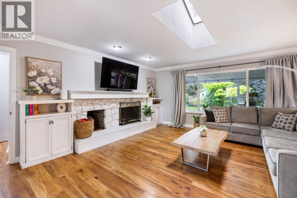 Living room featuring a stone fireplace, a large sectional sofa, a wooden coffee table, and a skylight. - 21678 Mountainview Crescent, Maple Ridge