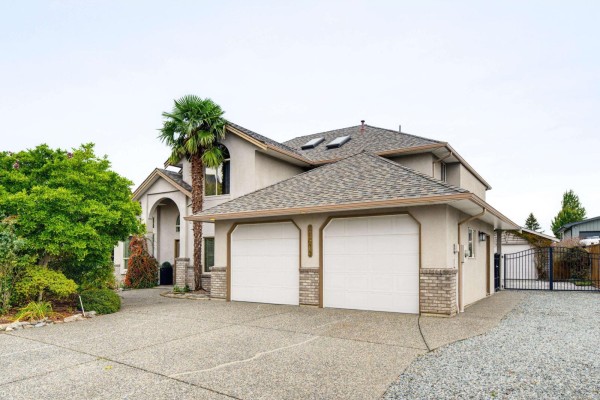 Exterior view of a stucco house with a tan facade, grey shingle roof, and a three-car garage. - 21679 52 Avenue, Langley