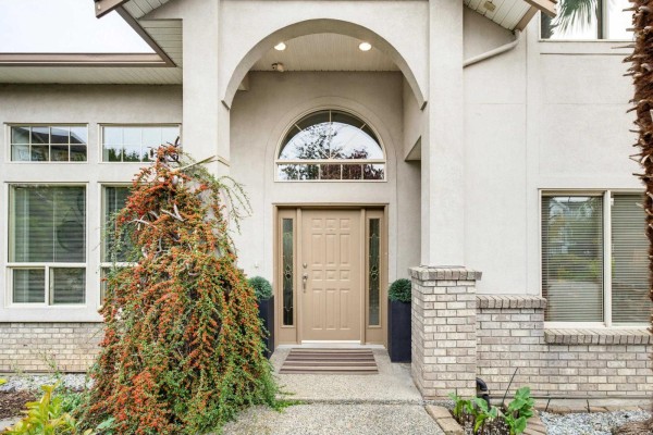 Front entrance of the house features a beige front door with glass panels, arched entryway, and brick accents. - 21679 52 Avenue, Langley