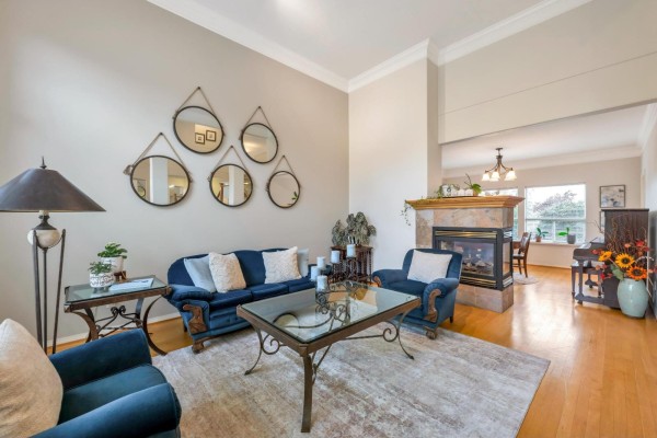 Living room with a fireplace, blue velvet sofa and chairs, glass coffee table, and adjacent dining area with piano. - 21679 52 Avenue, Langley