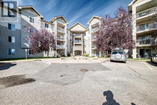 Exterior view of apartment building entrance with trees and parking. - 217, 2000 Somervale Court Sw, Calgary