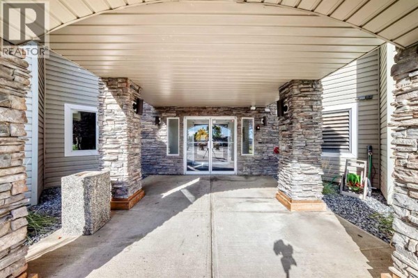 Covered entrance with stacked stone pillars leading to glass double doors. - 217, 2000 Somervale Court Sw, Calgary