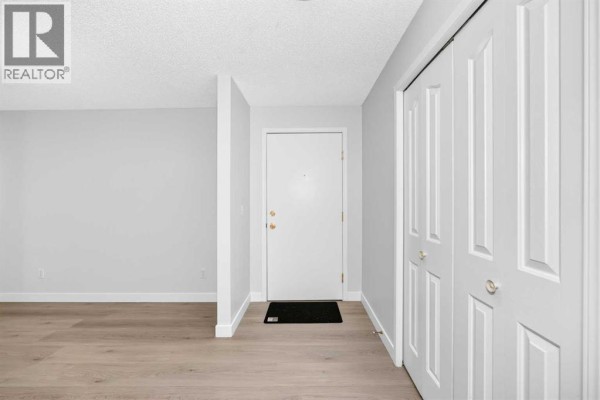 Empty hallway with a white door, light grey walls, and double white doors. - 217, 2000 Somervale Court Sw, Calgary