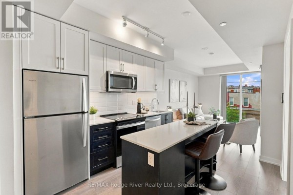 Open-concept kitchen with stainless steel appliances, island, and adjacent living area. - 217 - 201 Brock Street S, Whitby