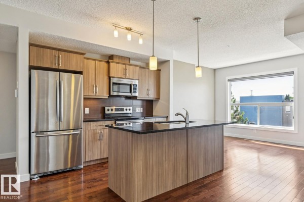 Kitchen featuring wood cabinetry, black countertops, and stainless steel appliances. - #217 10523 123 St Nw, Edmonton