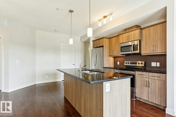 Kitchen island with sink and dark granite countertop, adjacent to living space. - #217 10523 123 St Nw, Edmonton