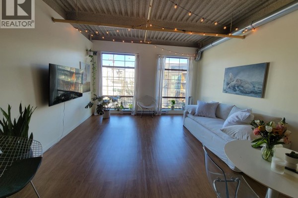 Living room with white sofa, large windows, and exposed ceiling. - 217 237 E 4th Avenue, Vancouver