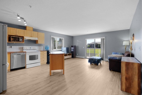 Apartment living space with kitchen, island, sofa, and sliding glass door to balcony with view. - #217 240 Spruce Ridge Rd, Spruce Grove